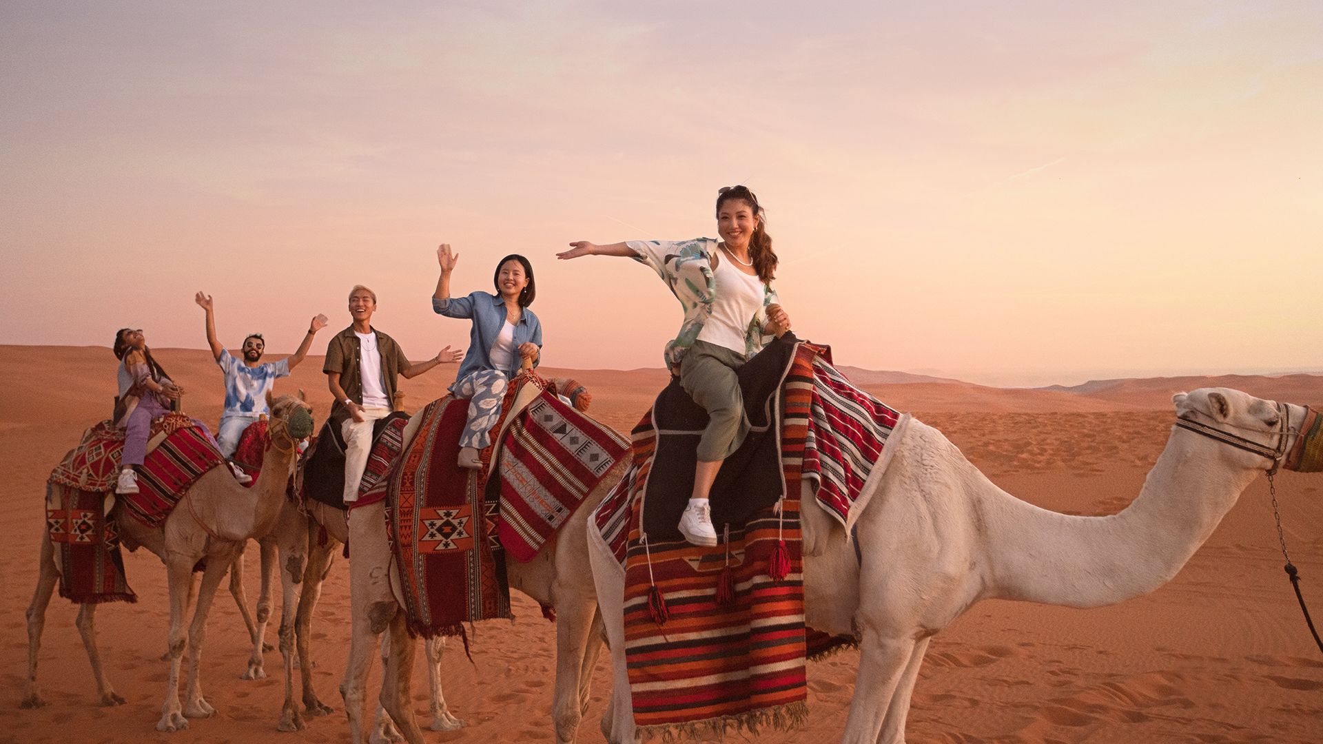 Four people riding camels across a desert landscape    
